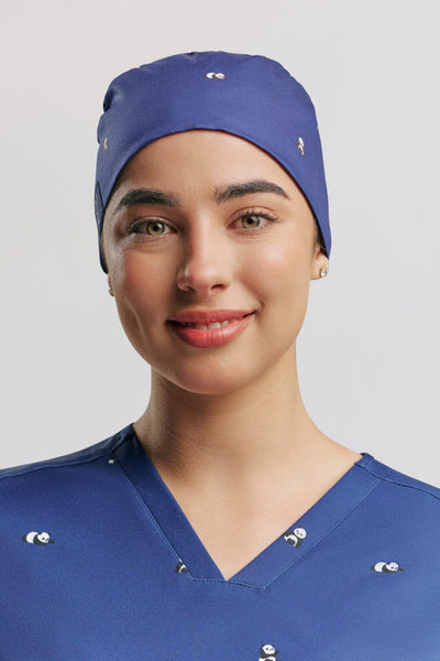 Frontal portrait of a smiling female healthcare worker in blue scrubs wearing a blue tie-back scrub cap, both printed with small panda illustrations.