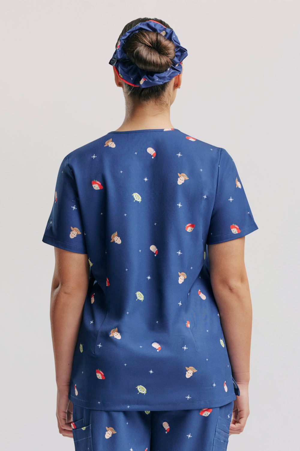 Direct rear view of nurse wearing the dark blue Disney & Pixar Toy Story Christmas scrub top and matching patterned scrub cap.  
