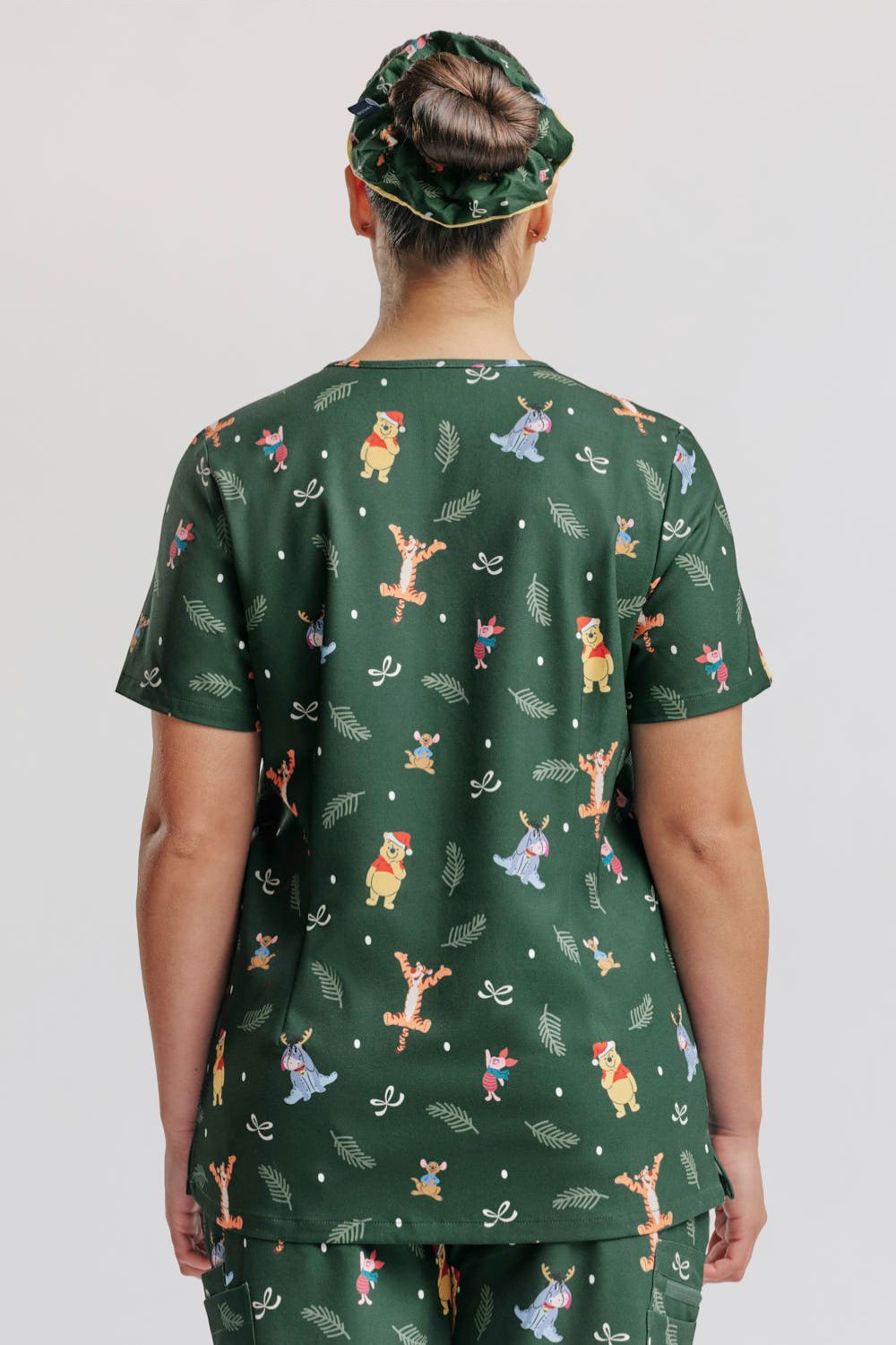 Direct rear view of a nurse wearing the dark forest green Winnie the Pooh scrub top, matching pants, and patterned scrub cap.