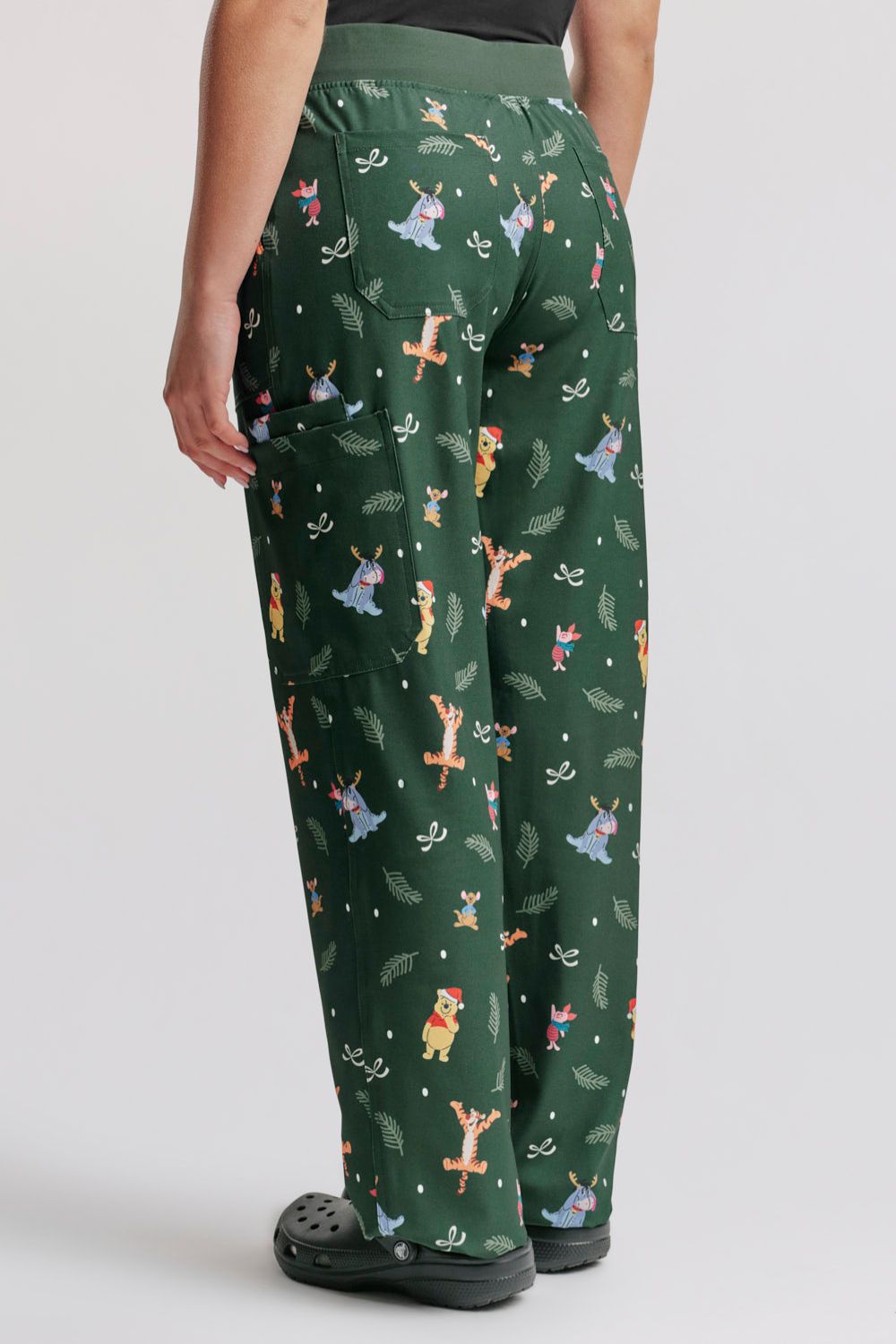 Direct rear view showing the leg drape, waist band fit, and pattern layout on the back of the dark forest green Winnie the Pooh scrub pants.