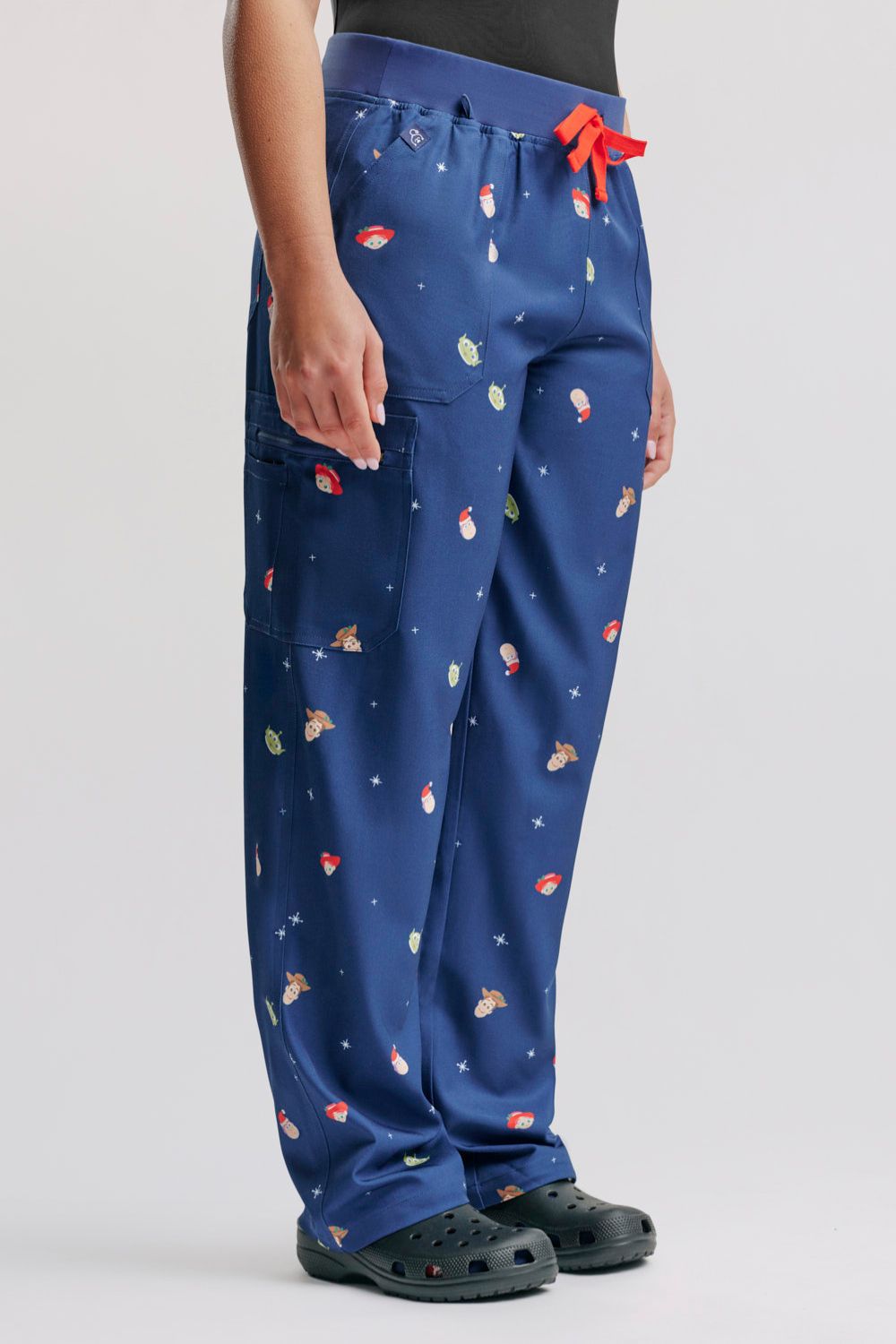 Side profile of a doctor wearing the dark blue Toy Story Christmas cargo scrub pants, highlighting the side pocket placement and leg fit, styled with dark grey Clogs.