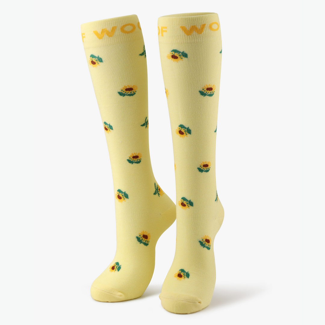 Pair of light yellow compression socks with sunflower print standing against a plain background.