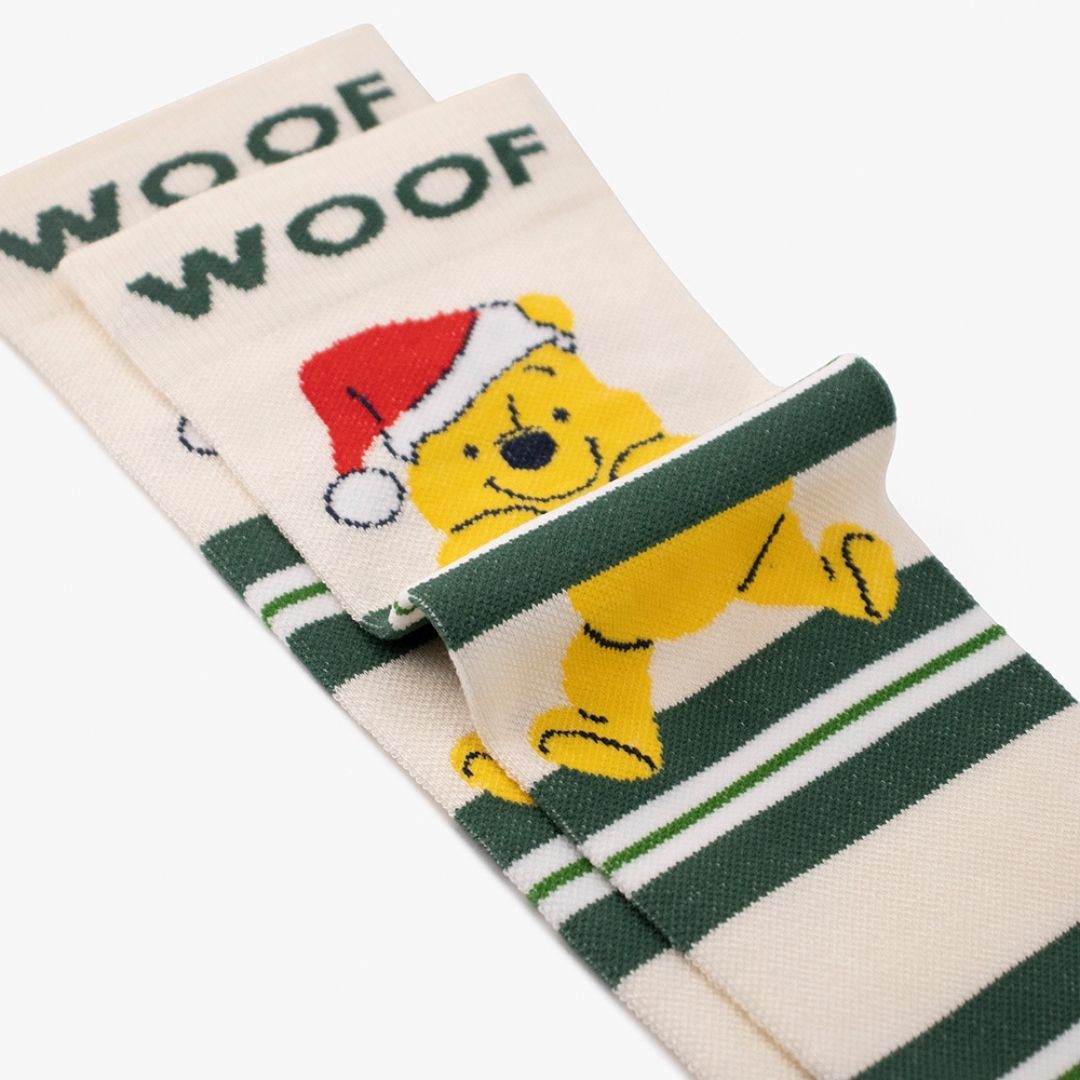 A Winnie The Pooh Christmas Bamboo Crew Compression Socks folded neatly to highlight the dark green woven "WOOF" cuff bands, the Santa hat-wearing Pooh graphic, and the striped knit pattern layout.  