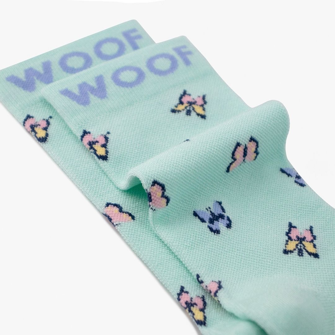 A Butterfly Bamboo Crew Compression Socks folded neatly to highlight the purple woven "WOOF" cuff bands and the butterfly knit pattern layout.