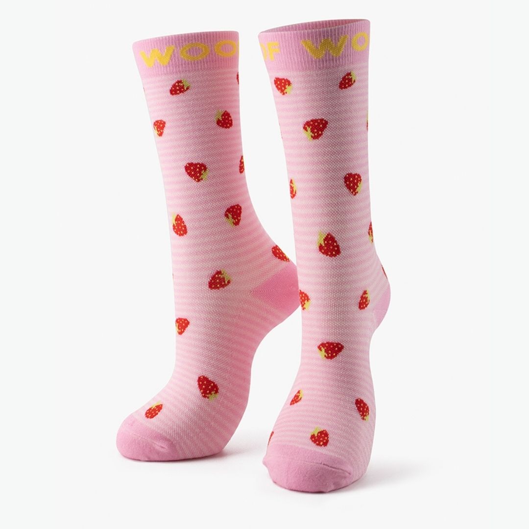 A pair of light pink Strawberries Bamboo Crew Compression Socks standing upright, featuring subtle horizontal texturing, scattered red strawberry motifs, and yellow "WOOF" woven into the top cuffs.  