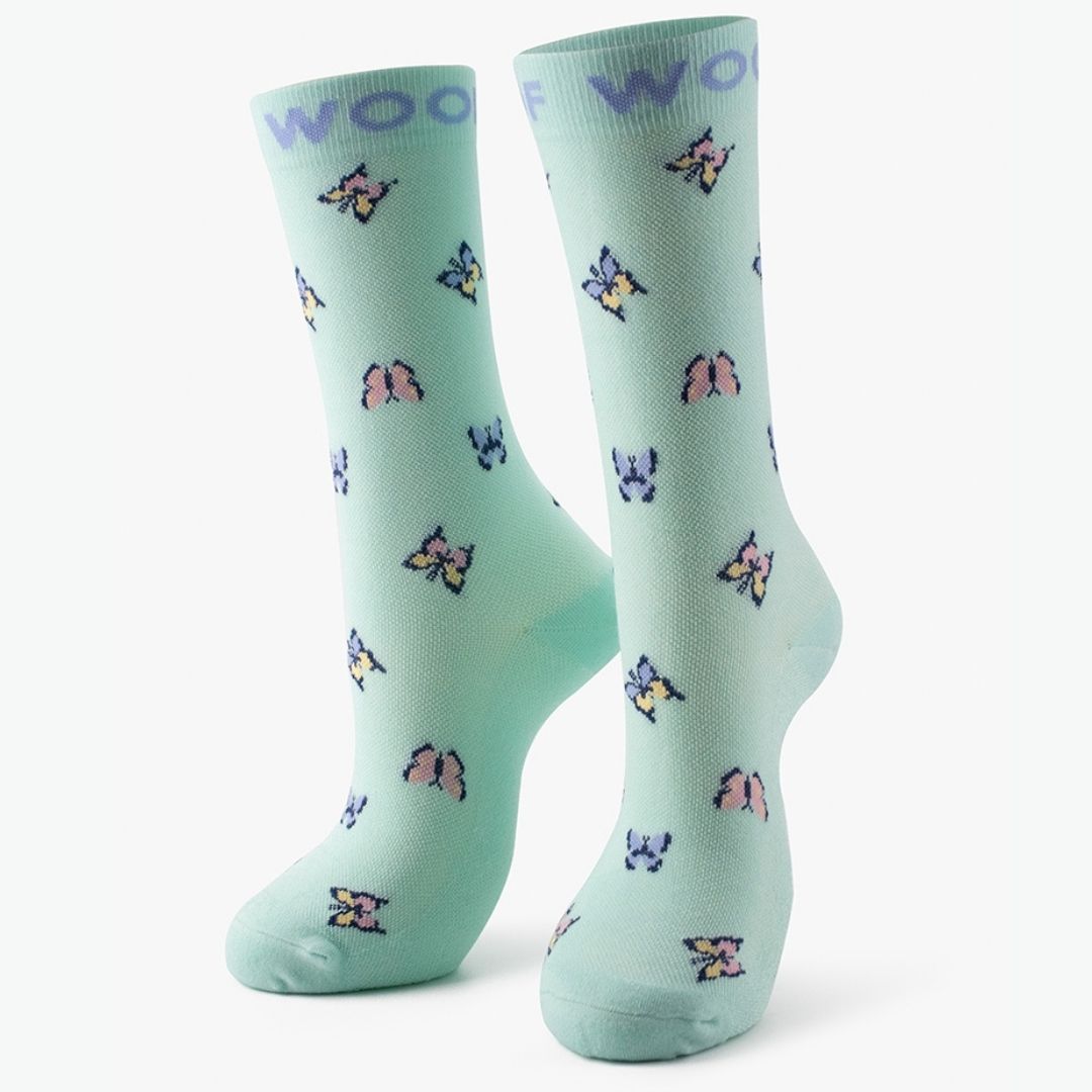 The pair of mint green Butterfly Bamboo Crew Compression Socks standing upright, featuring multi-colored pastel butterfly motifs with purple "WOOF" woven into the top cuffs.