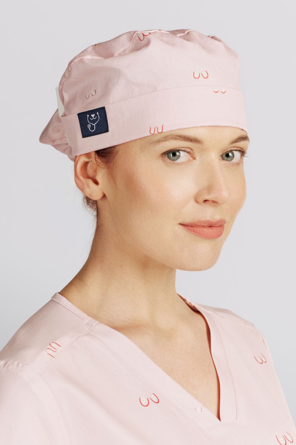 Side profile of a doctor wearing a light pink scrub cap with line art small boobs print.