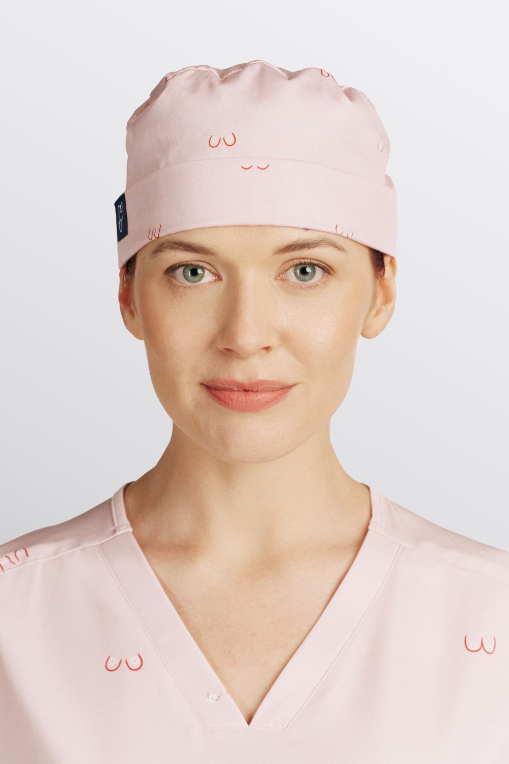 Front view of a nurse wearing a light pink scrub cap with line art small boobs print.