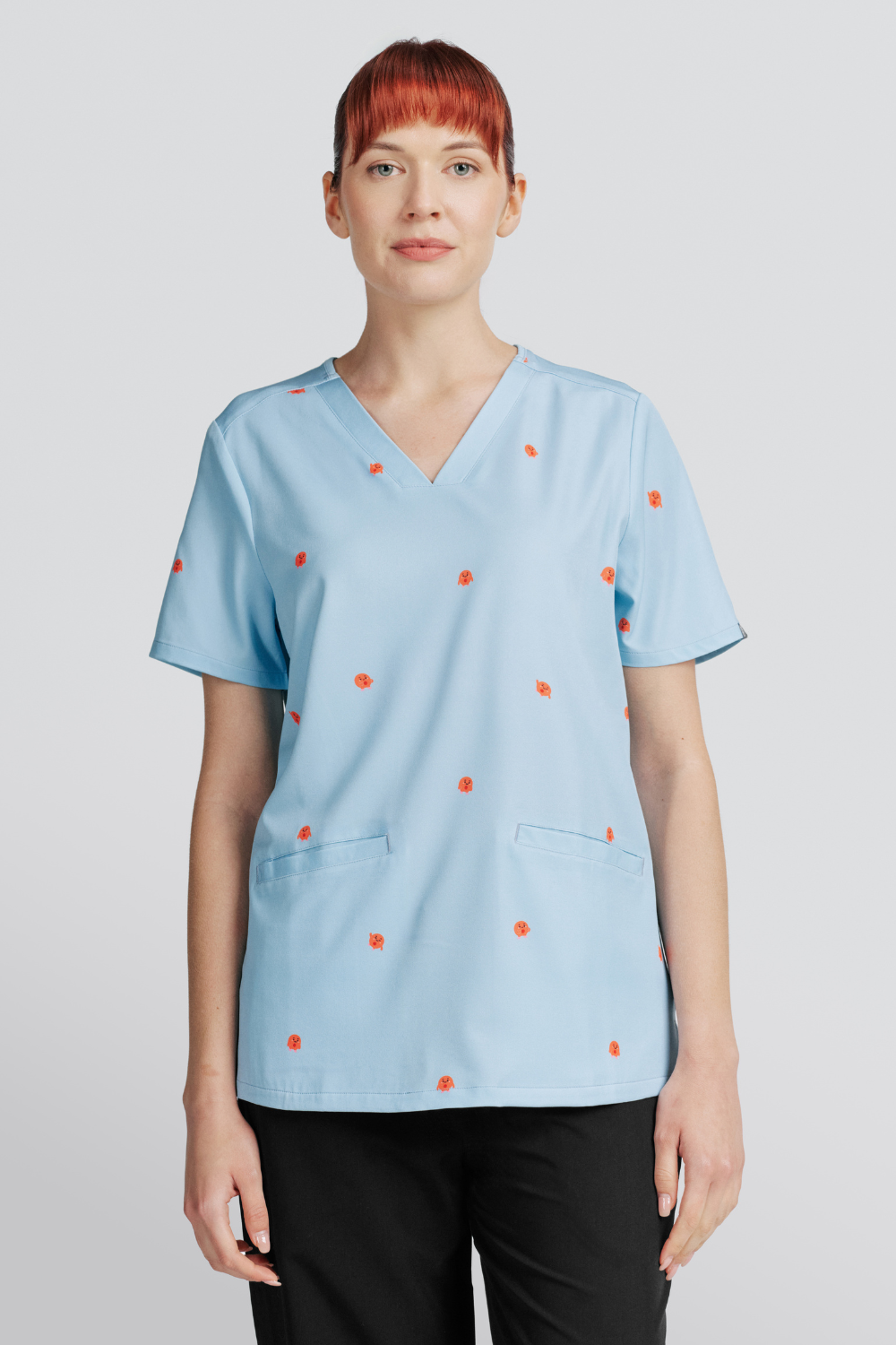 Front view of a veterinarian wearing a light blue scrub top with cute red blood cells print and front pockets.