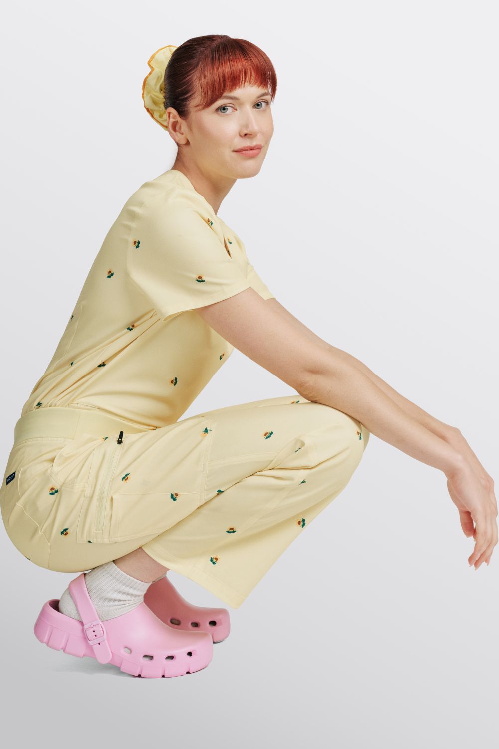 Veterinarian crouching in a light yellow scrub set with mental health sunflower print and pink clogs.
