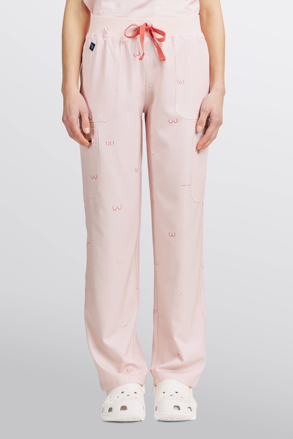 Front view of a doctor wearing light pink scrub pants with line art small boobs print and white clogs.