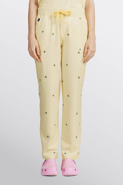 Front view of light yellow scrub pants with sunflower print and drawstring waistband worn with pink clogs.