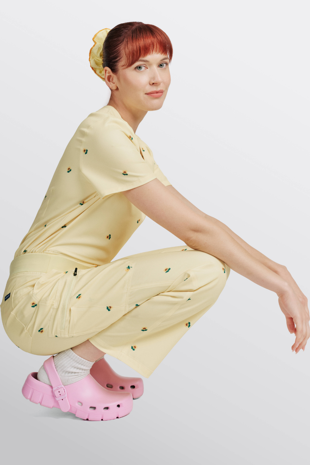 Nurse crouching in light yellow scrub pants with sunflower print and matching top.
