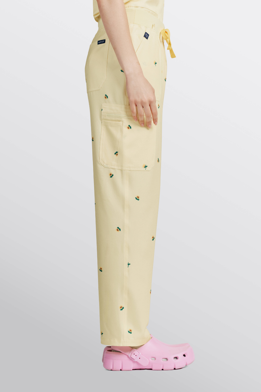 Side profile of a vet nurse wearing light yellow scrub pants with sunflower print and pink clogs.