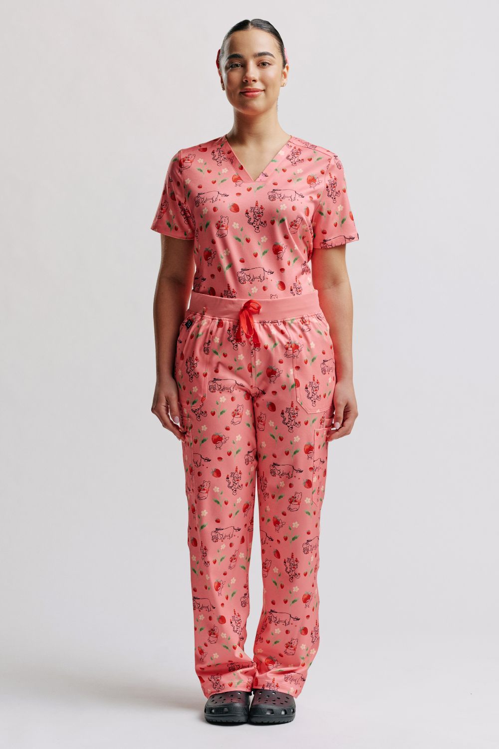 Doctor standing in full light pink scrub set with Winnie the Pooh strawberry print and black clogs.