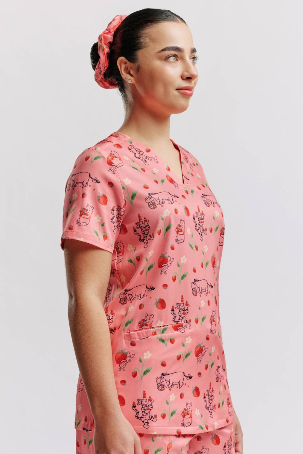 Side profile of a vet nurse wearing a light pink scrub top with Winnie the Pooh strawberry print and matching scrunchie.