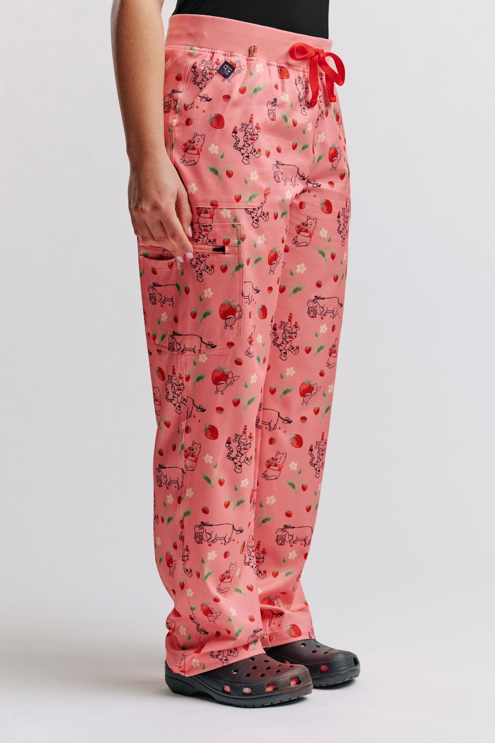 Side profile of a vet nurse wearing light pink scrub pants with Winnie the Pooh strawberry print and black clogs.