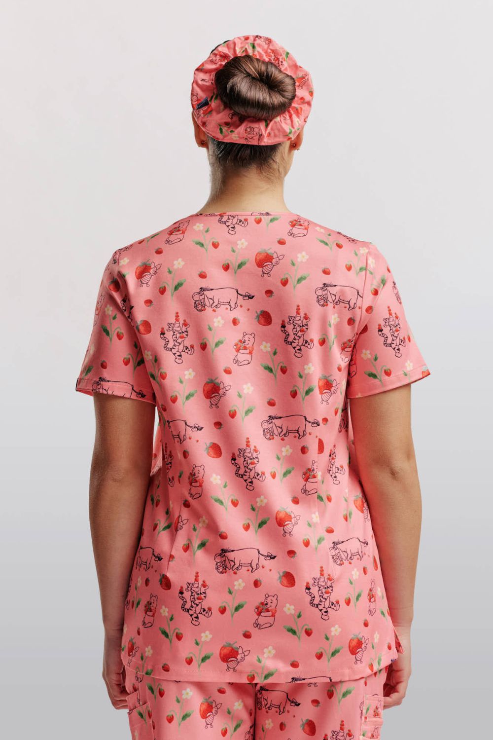 Back view of a dentist wearing a light pink scrub top with Winnie the Pooh strawberry print and matching scrub cap.