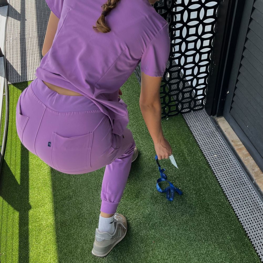 Person in purple attire crouching on artificial grass near a patterned screen.