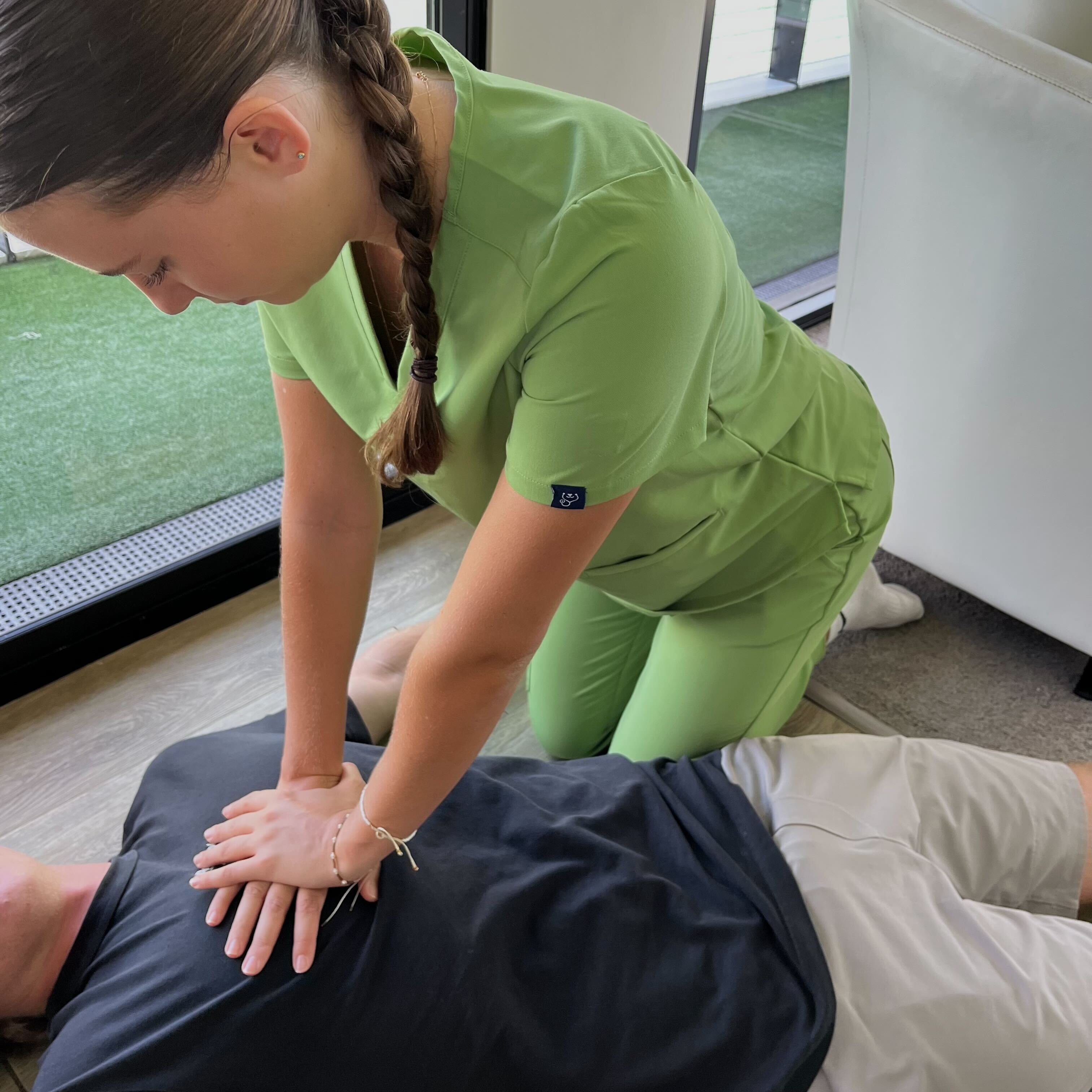 Person in green scrubs performing CPR chest compressions on someone lying on the floor.