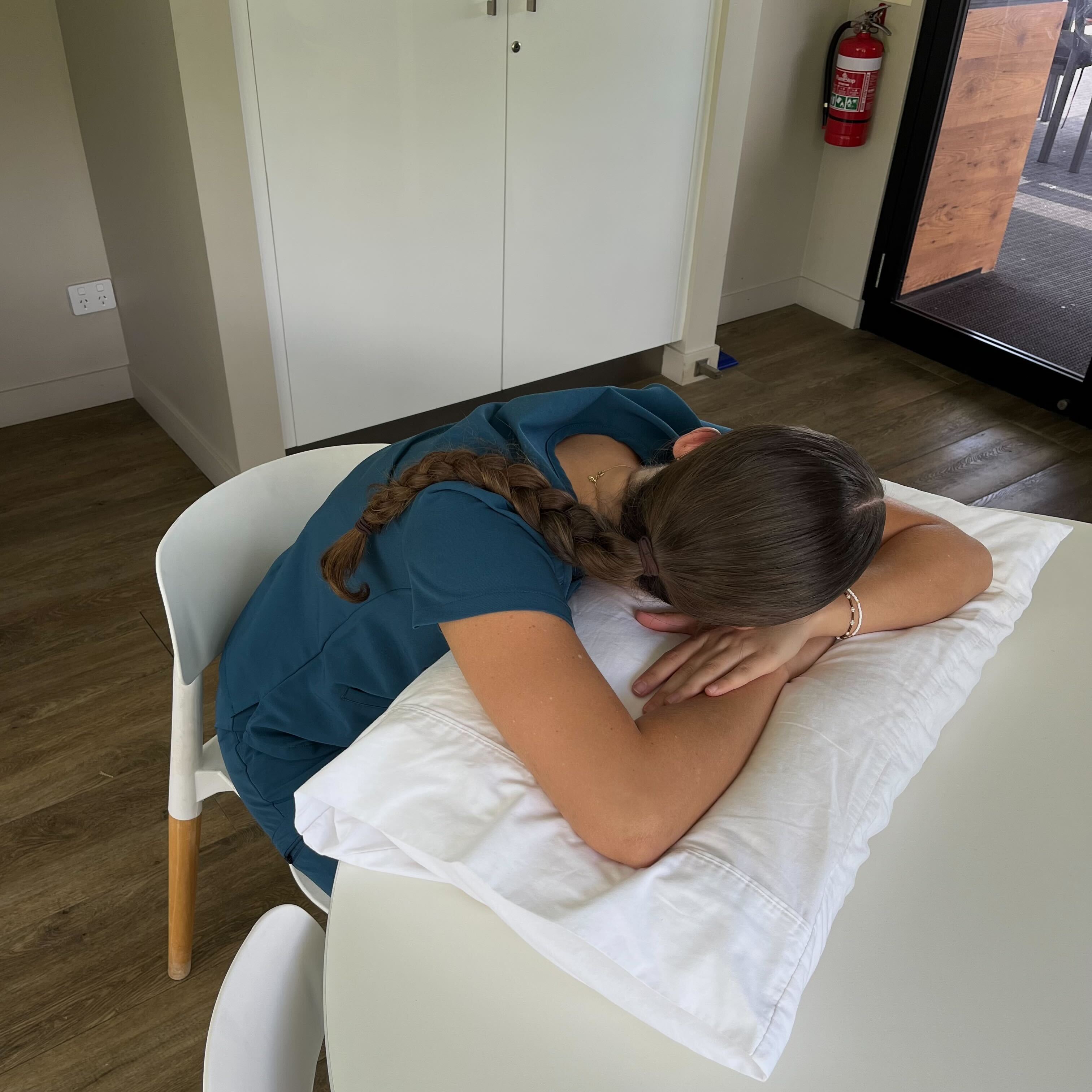 Person sleeping on a table with a pillow in a bright room.