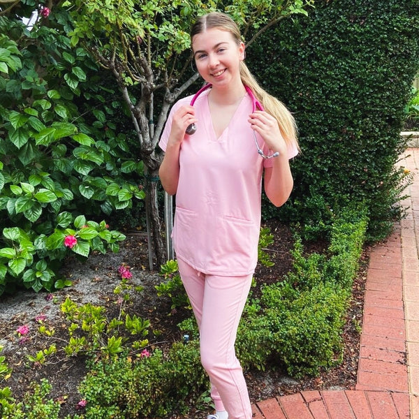 A med student in her garden wearing baby pink scrubs and a pink stethoscope