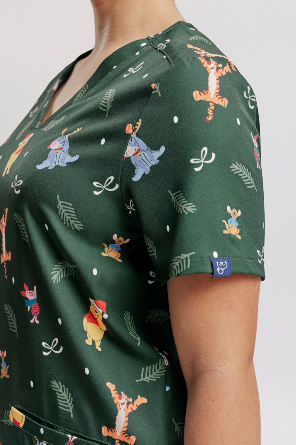 Close-up focusing on the neckline, shoulder drape, and sleeve fit of the dark forest green Winnie the Pooh scrub top.