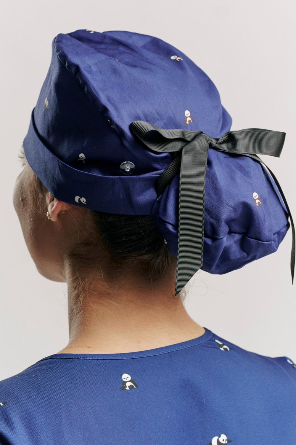 Direct rear view showing the fabric tie closure of the blue panda-print scrub cap paired with matching panda-print blue scrubs.