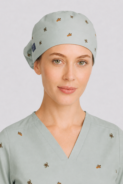 Close-up of a nurse wearing a light sage green scrub cap and matching v-neck scrub top with turtle design.