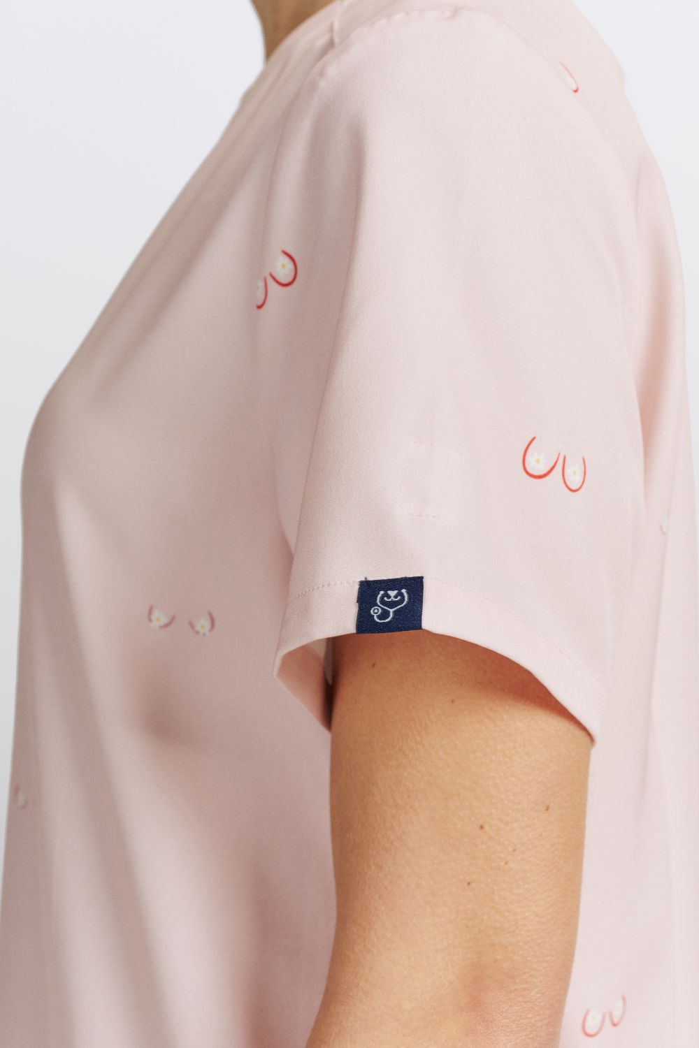 Close-up of a veterinarian wearing a light pink scrub top featuring sleeve detail and line art boobs print.