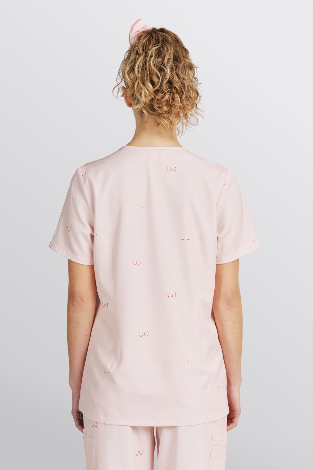 Back view of a vet nurse wearing a light pink scrub top with line art boobs print.