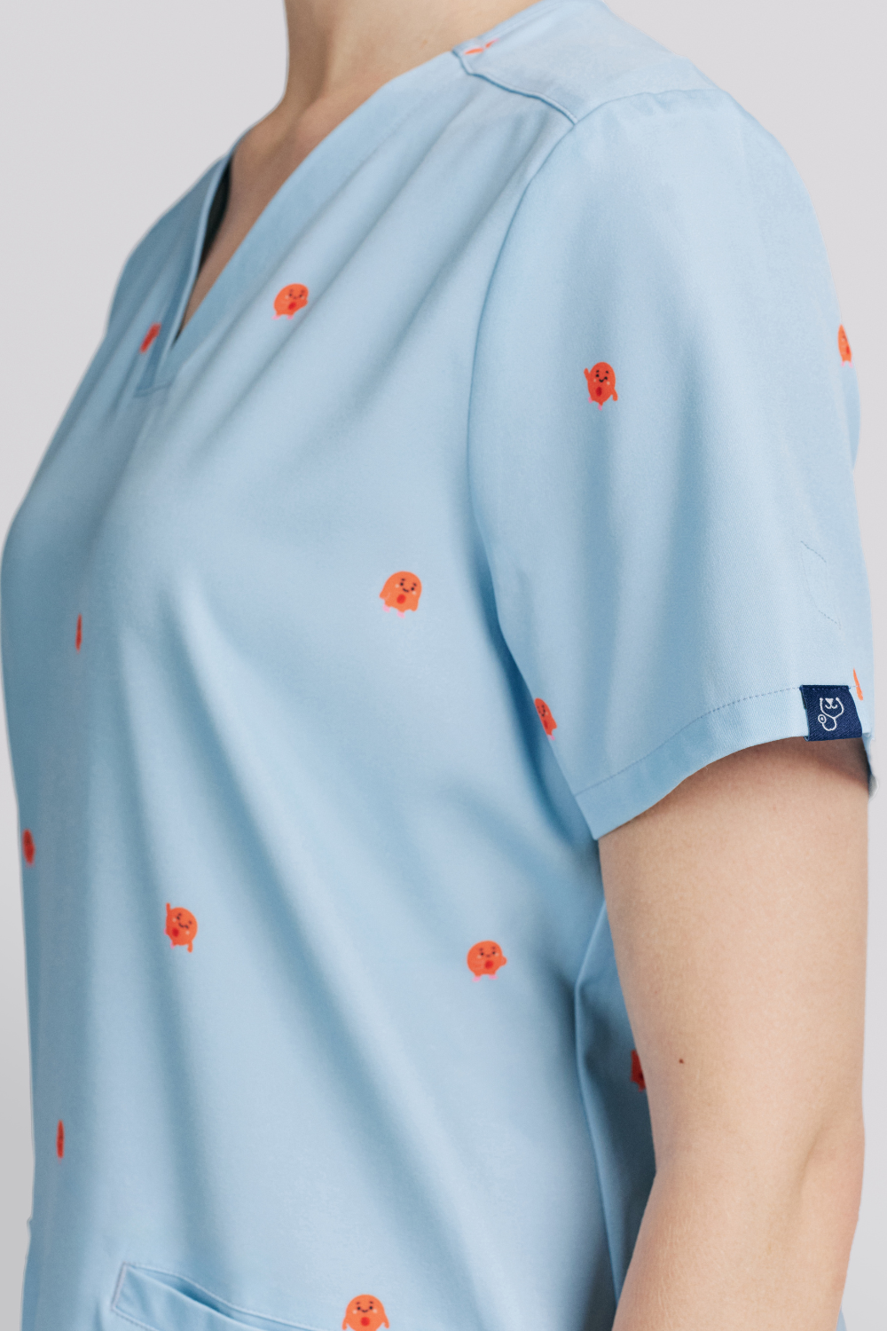 Close-up of a doctor wearing a light blue scrub top featuring a v-neckline and printed blood cells.
