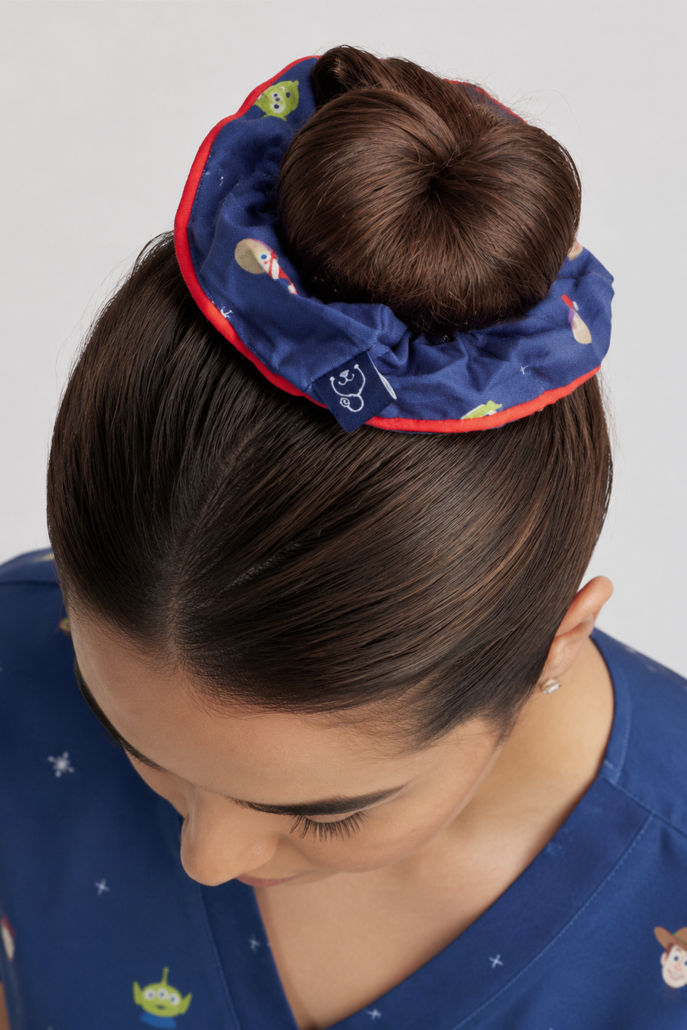 A royal blue Disney & Pixar’s Toy Story Women’s Scrunchie, Ho Ho Howdy featuring red piping trim and prints of Woody, Buzz Lightyear, and Little Green Aliens, paired with a matching blue scrub top.   